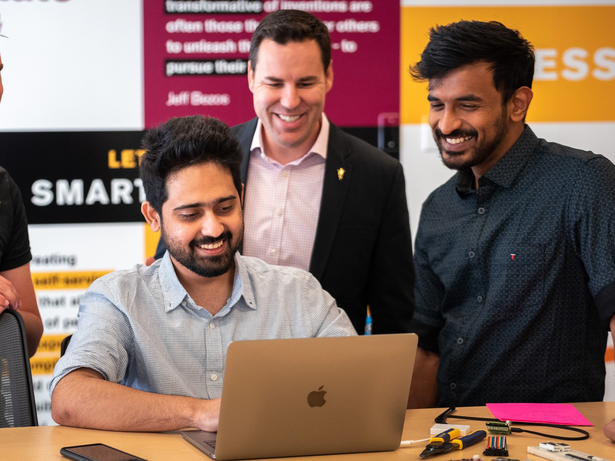 Three ASU employees working together on a laptop and smiling