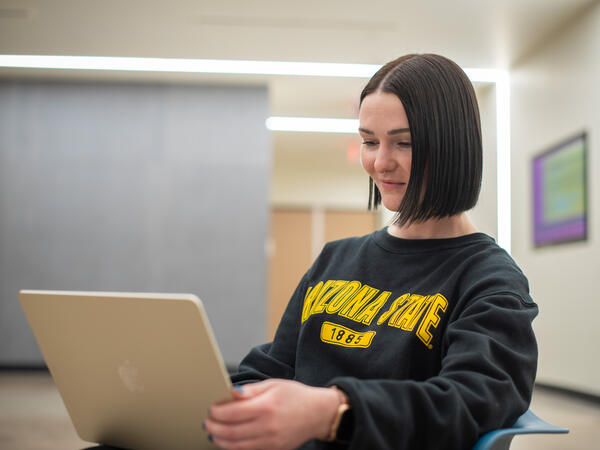 Student sitting with their laptop in their lap, wearing a Arizona State sweatshirt 