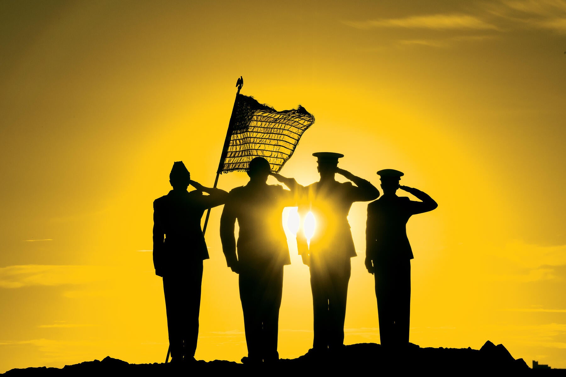 Four service members standing at salute with flag