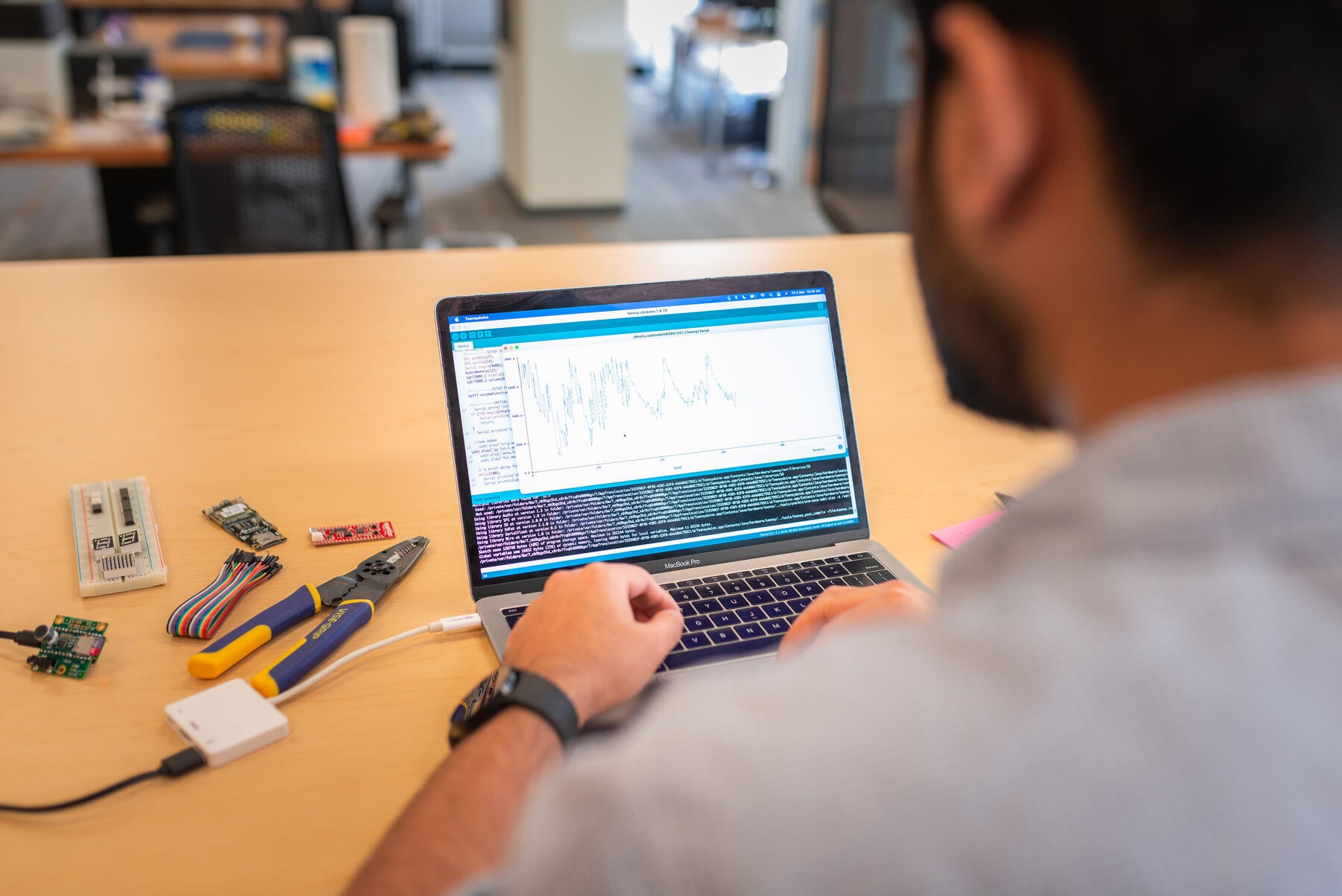 Student sitting at table with their back to the camera and computer on display with tools on the right side of table