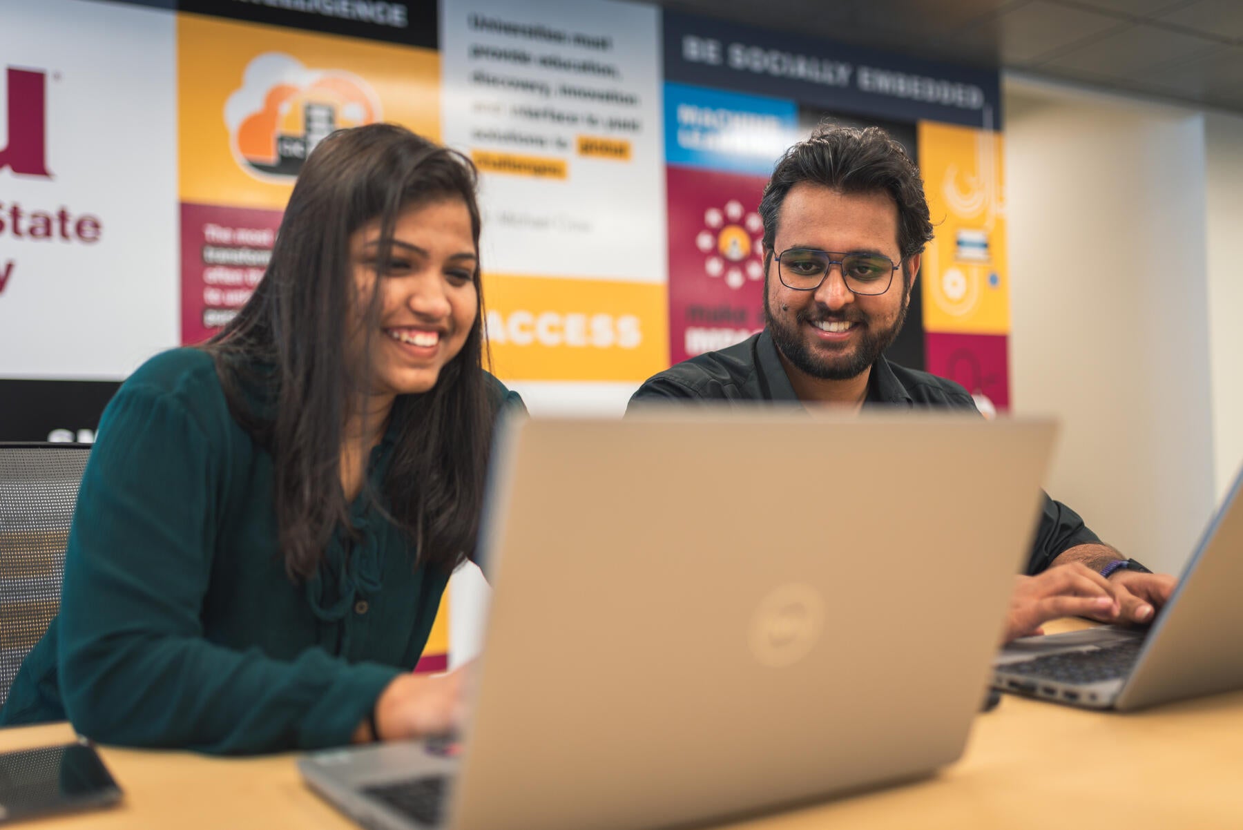 Two students working at their laptops while sitting. 