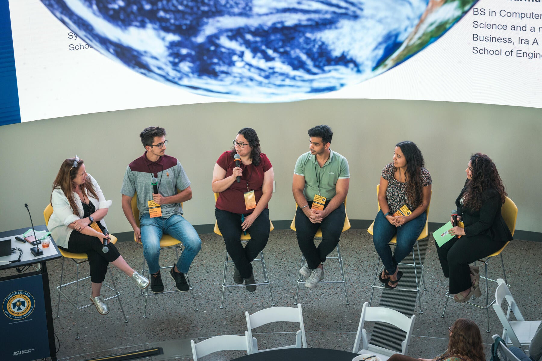 Top view of six people sitting people in chairs, each holding a hand held microphone.