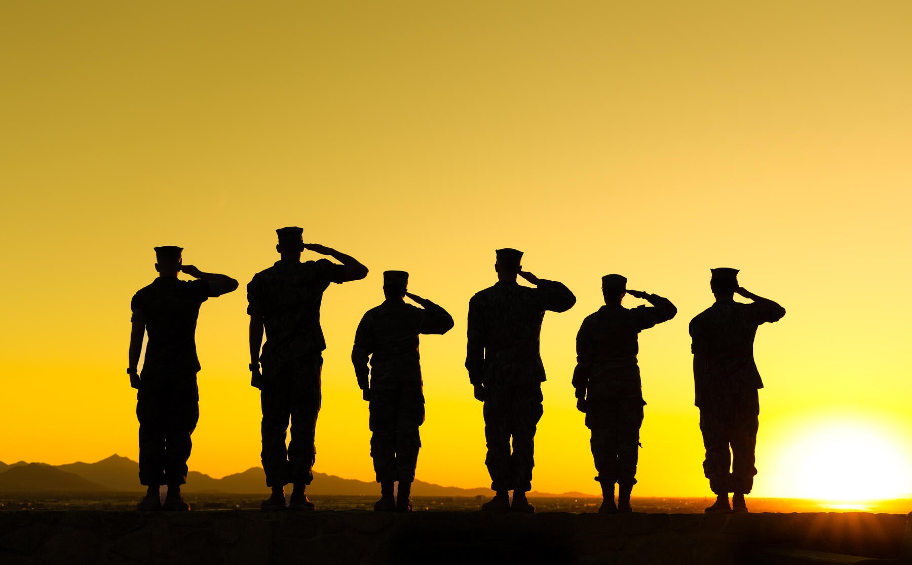 Six individuals raising their hands to their heads in military salute with gold background