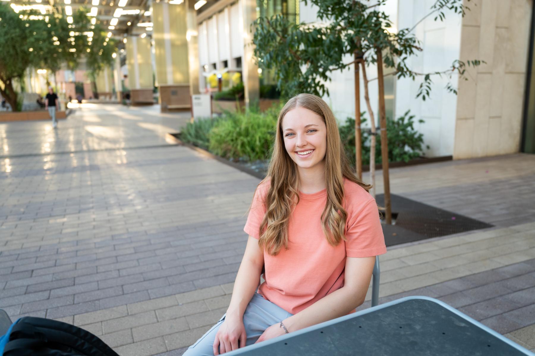 A student sitting at a table outside in an orange shirt