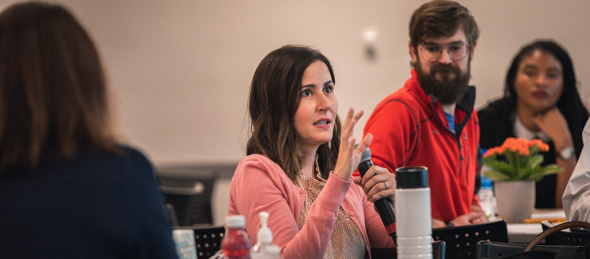 Person holding microphone while others at their table watch and listen