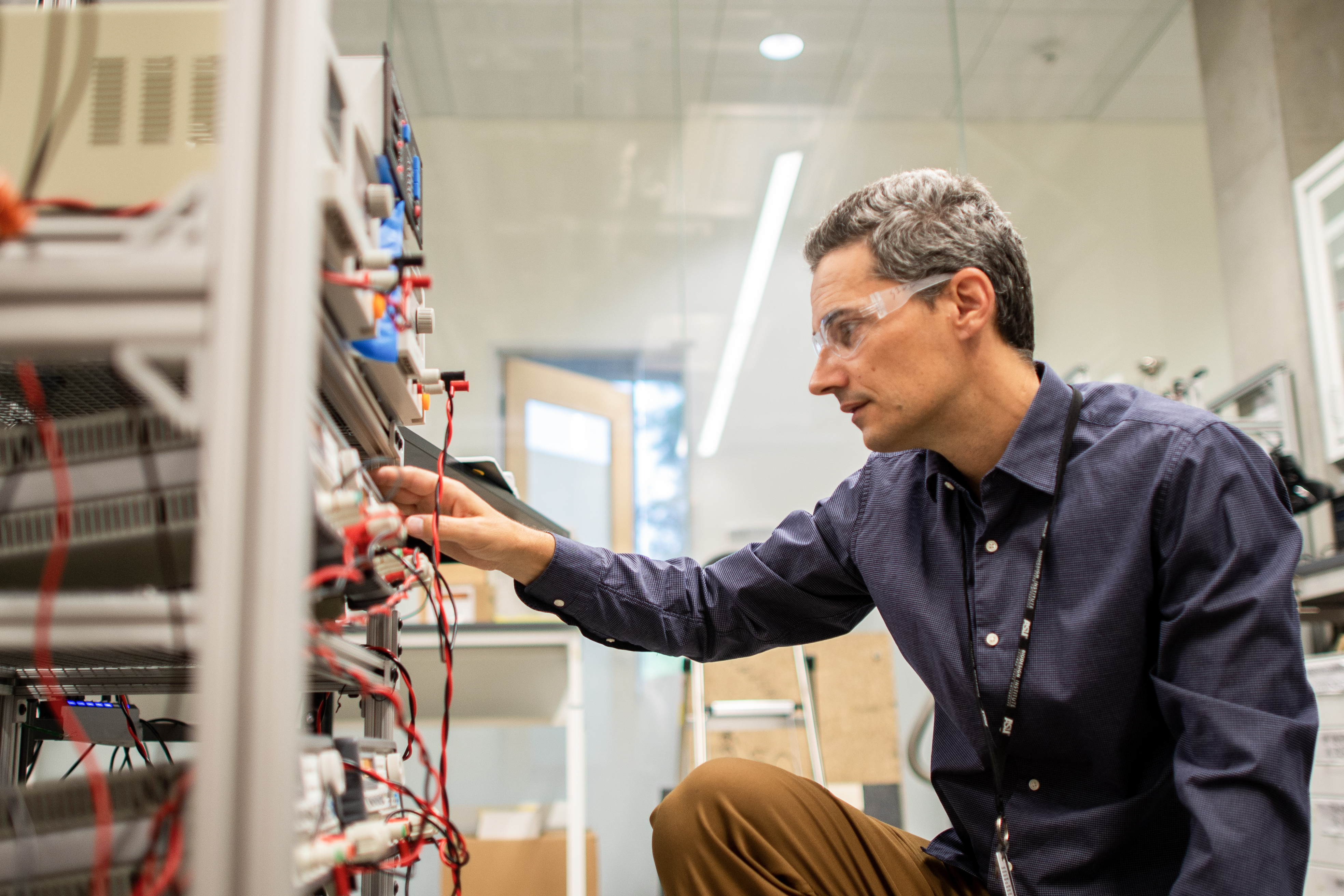 A man in goggles adjusts the wires of an electrical system pertaining to hydrogen research. 