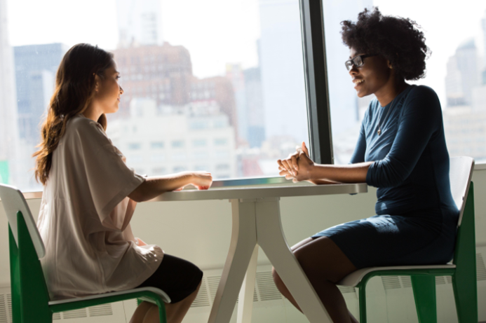 Two women speaking sitting on a table.