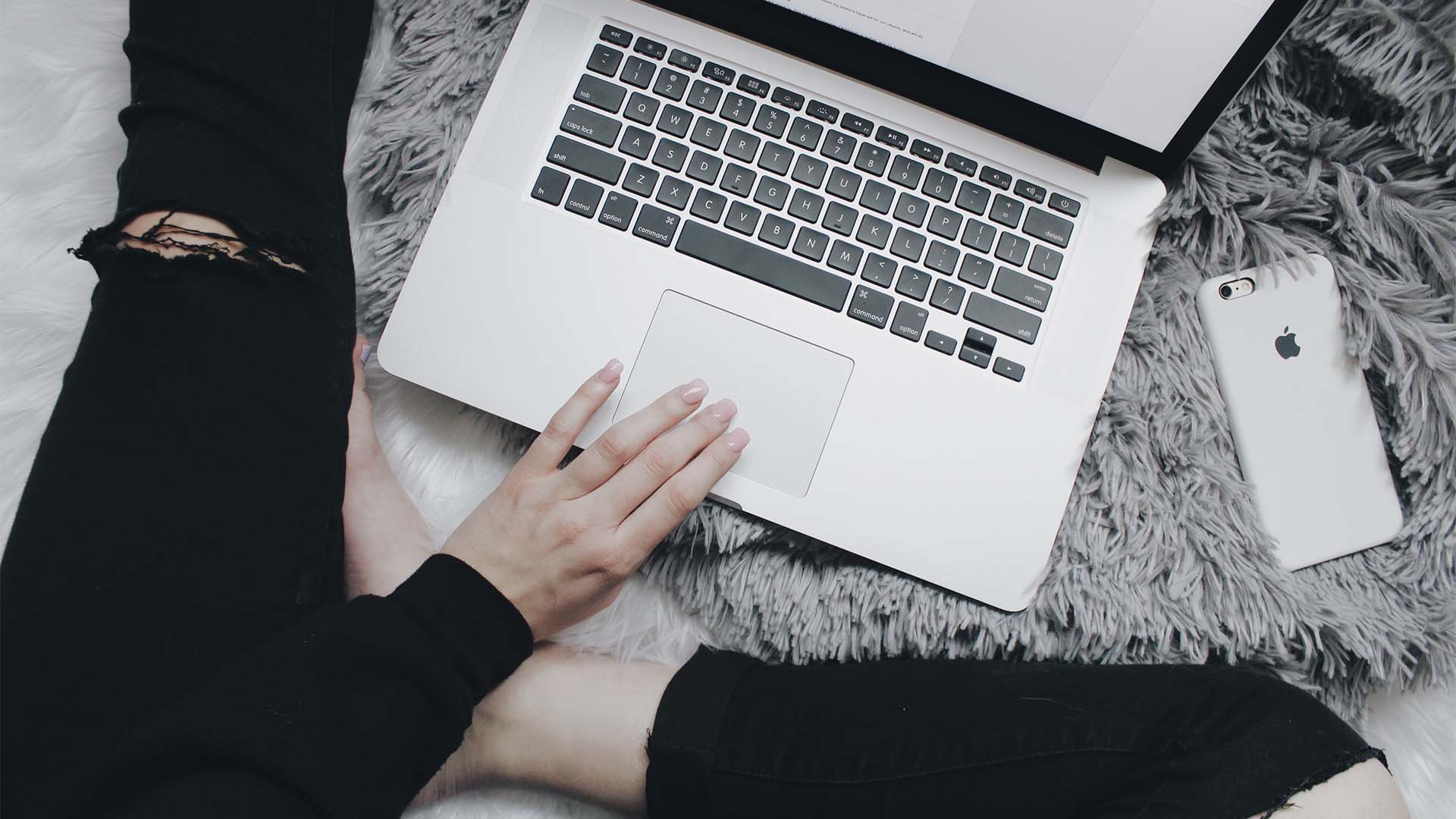 Someone's feet next to their laptop and phone on a bed or couch.