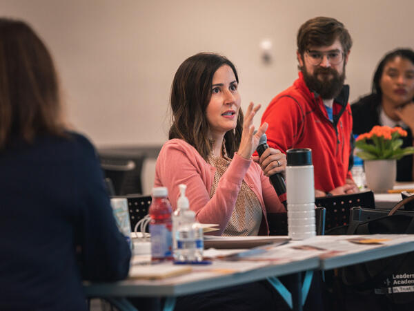 Person holding microphone while others at their table watch and listen