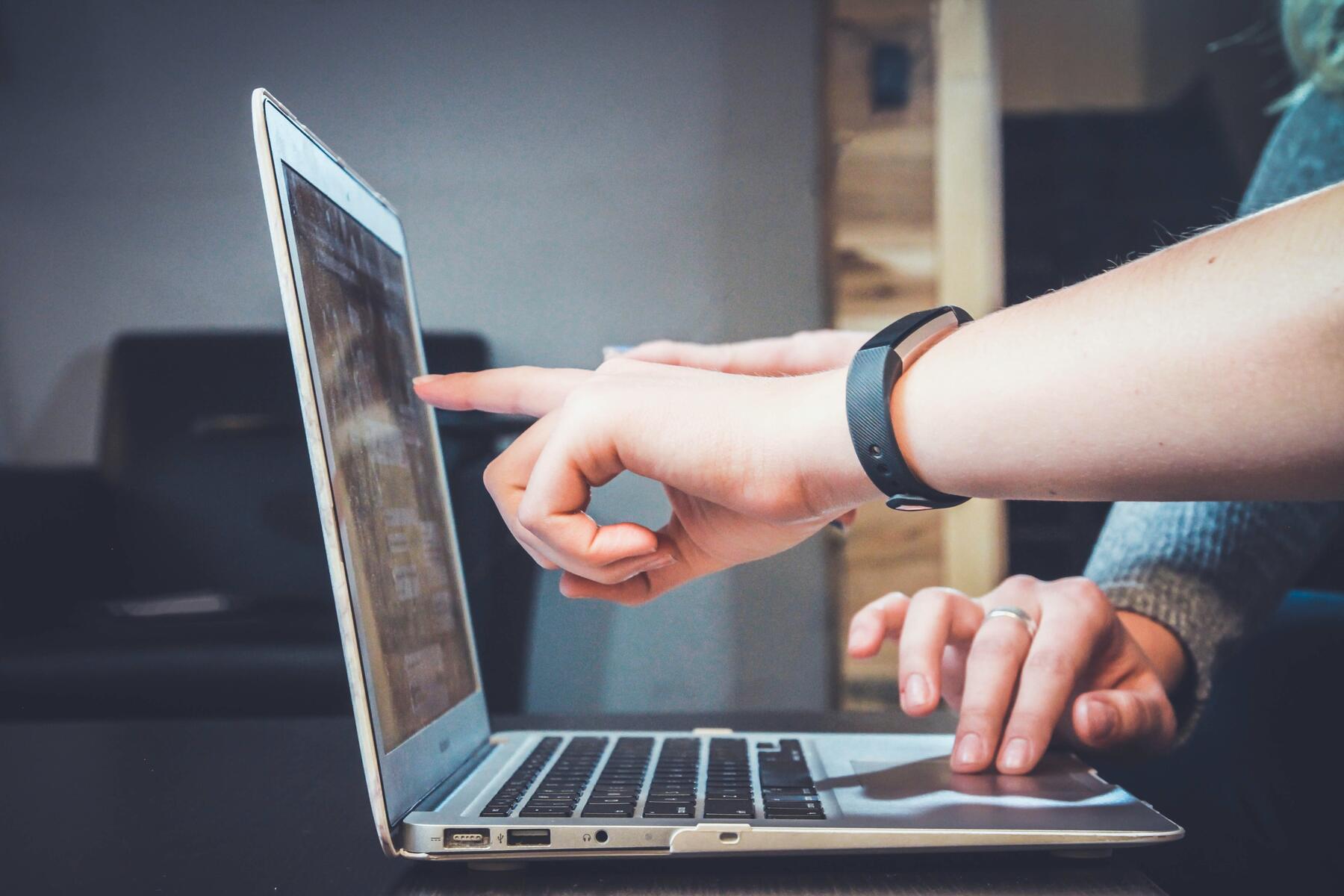 two people pointing at laptop working together