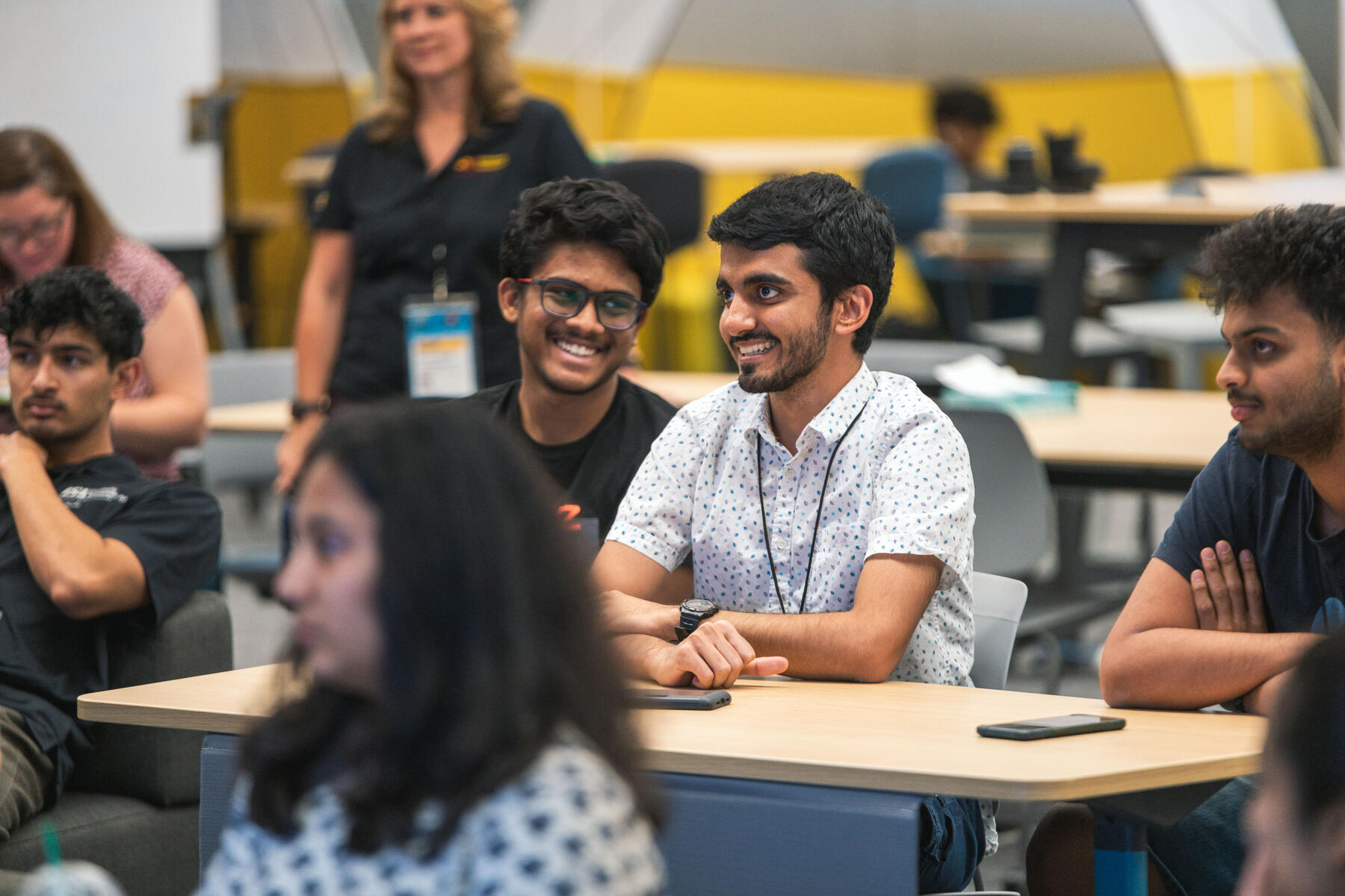 Two students smiling together at a table in a full room.