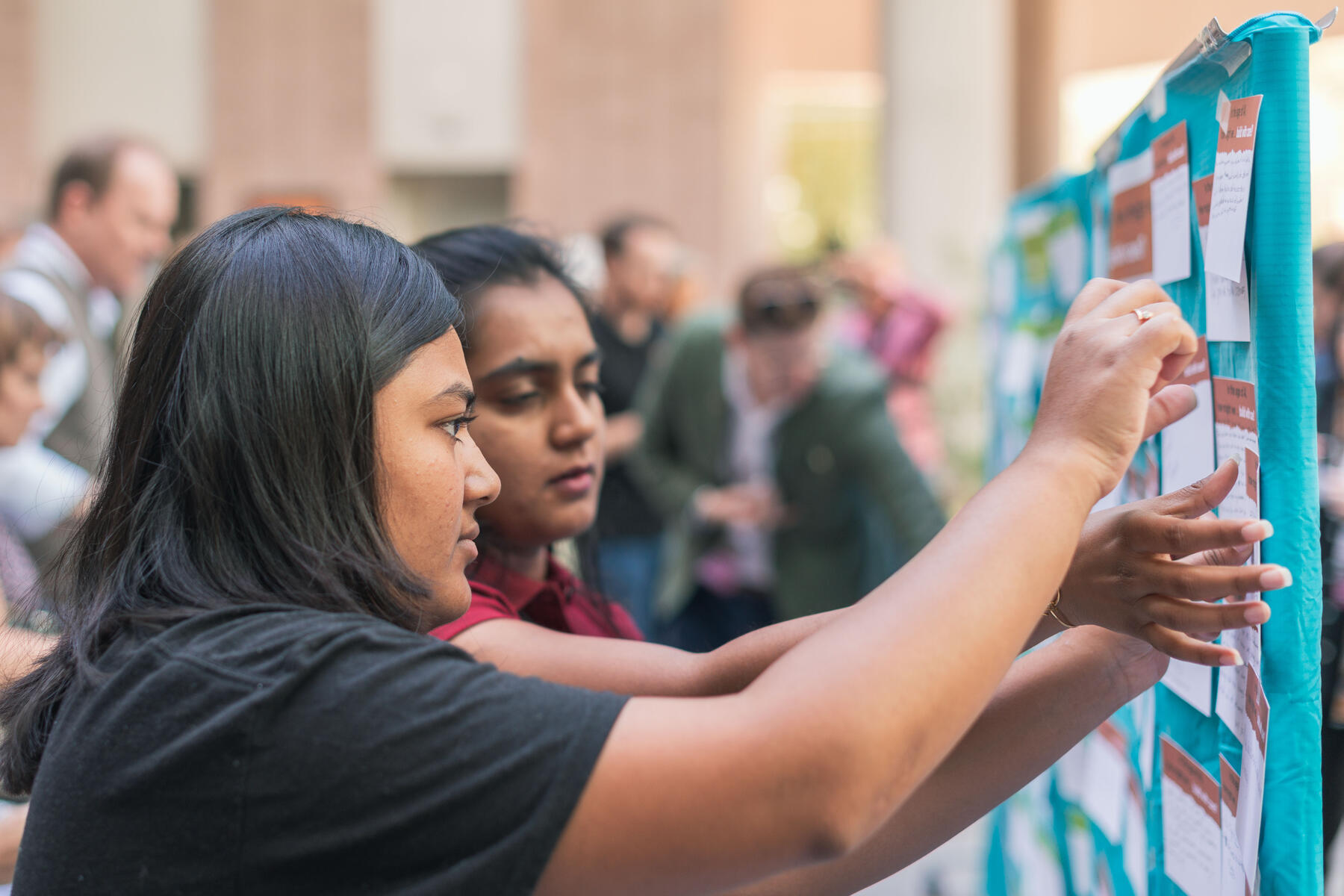 Two women standing at the activity board, pinning their notecards to the board. 