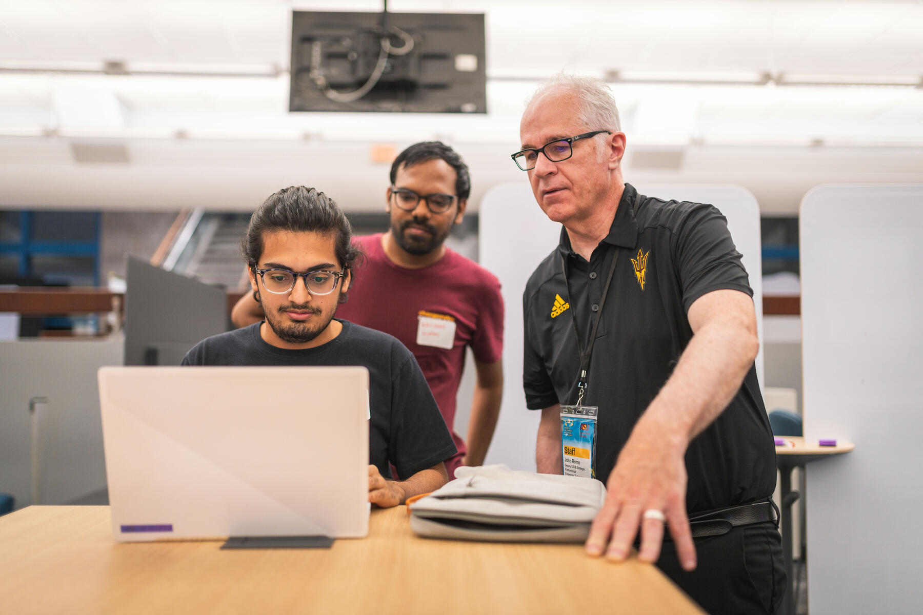 three men standing around a laptop computer