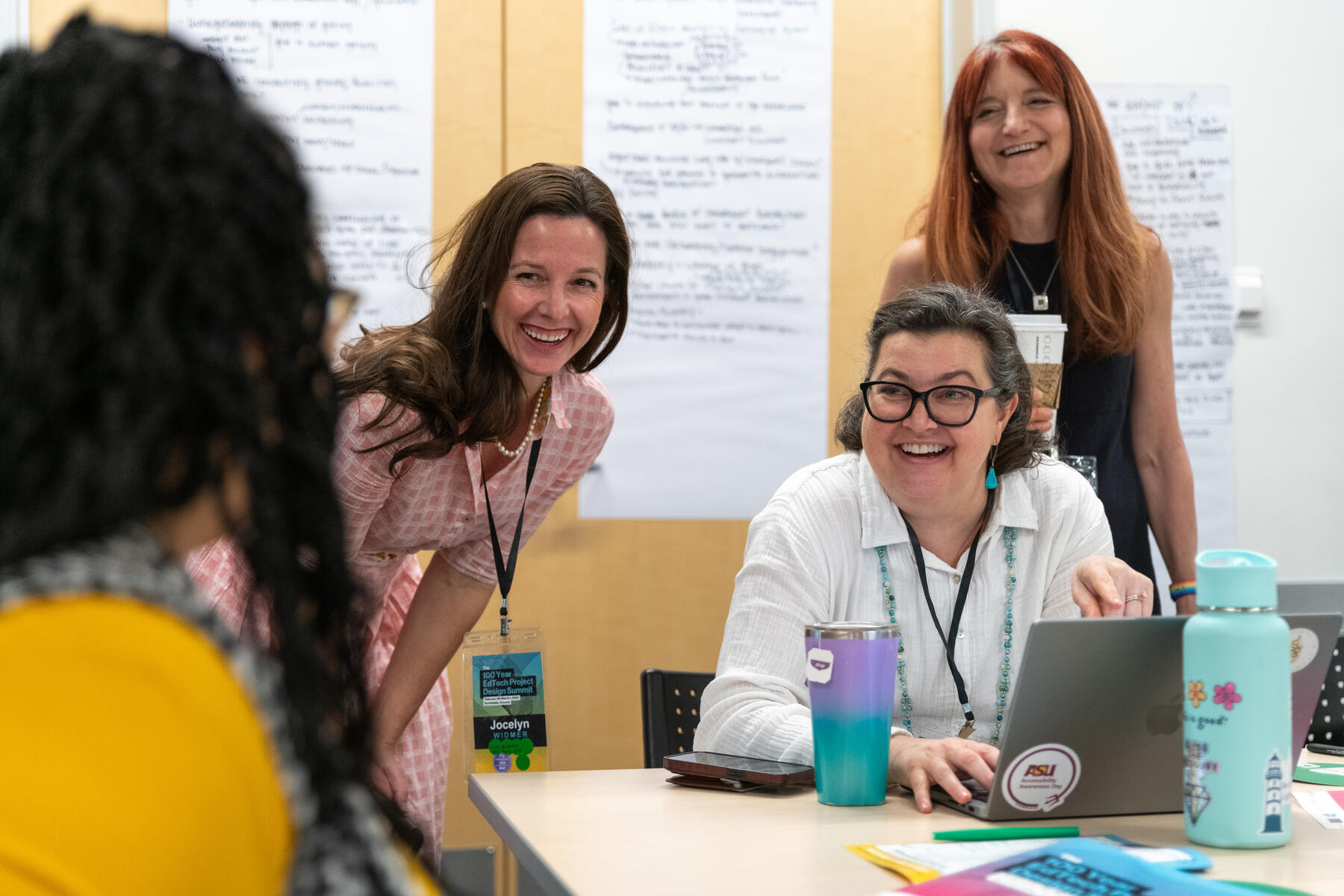 Three women smiling while talking with another colleague at the 100 Year EdTech Design Summit in 2024.