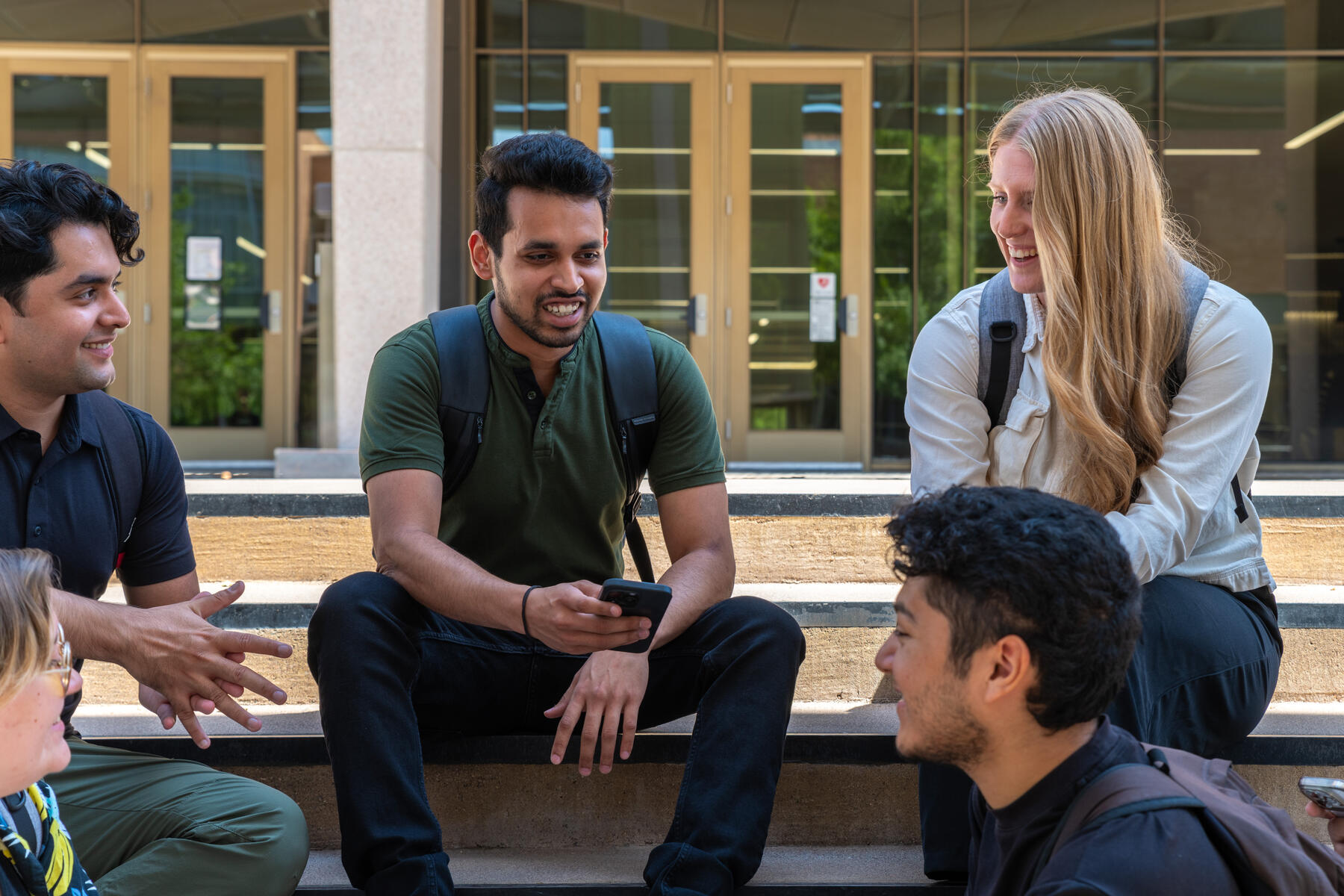 Students sitting together on the a set of steps outside looking down at their cell phones