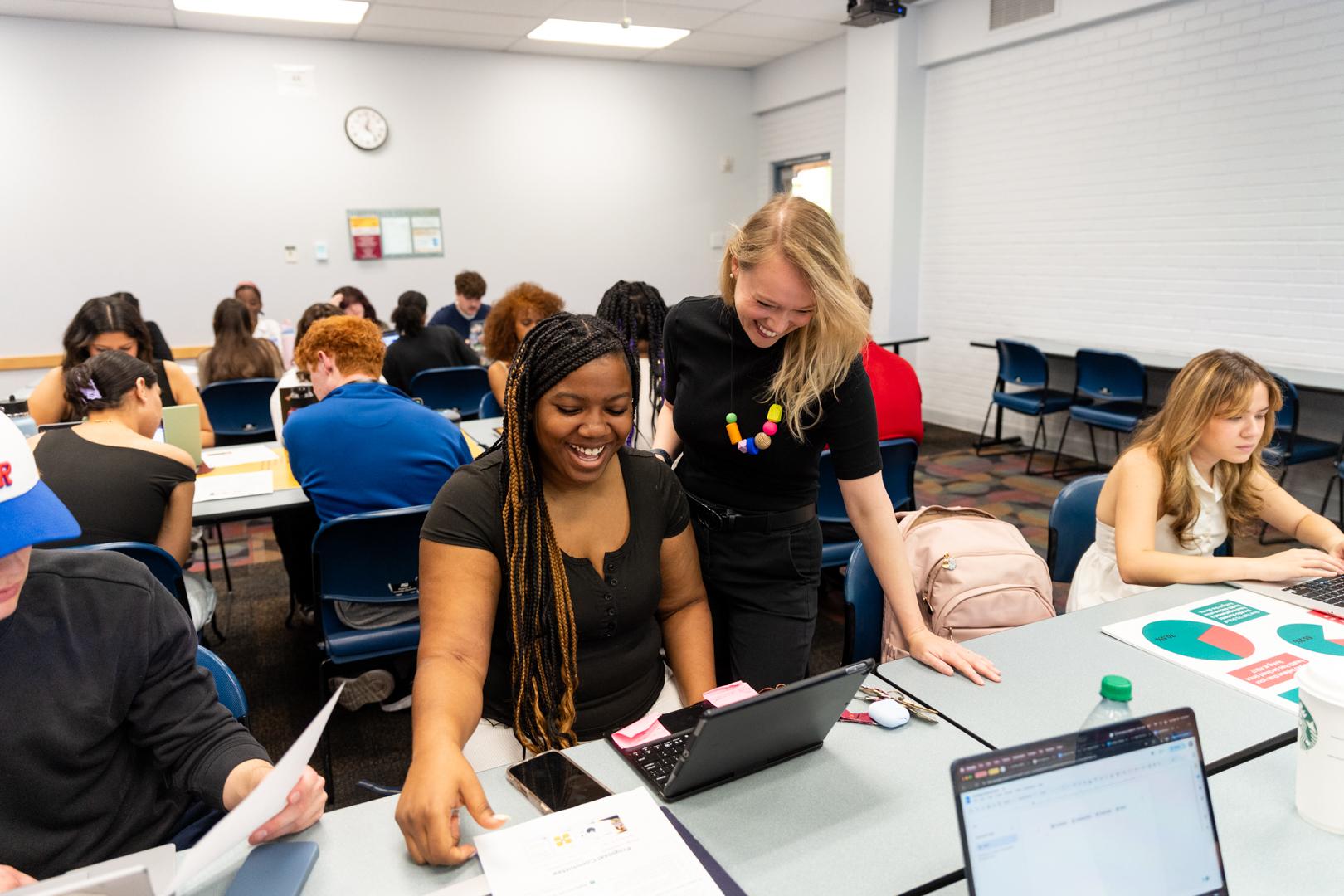 Teacher stands over seated student looking at laptop