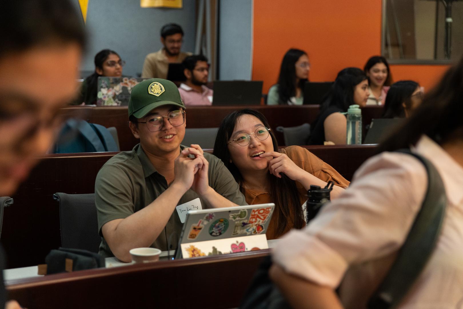 Two students seated in a crowded room looking ahead