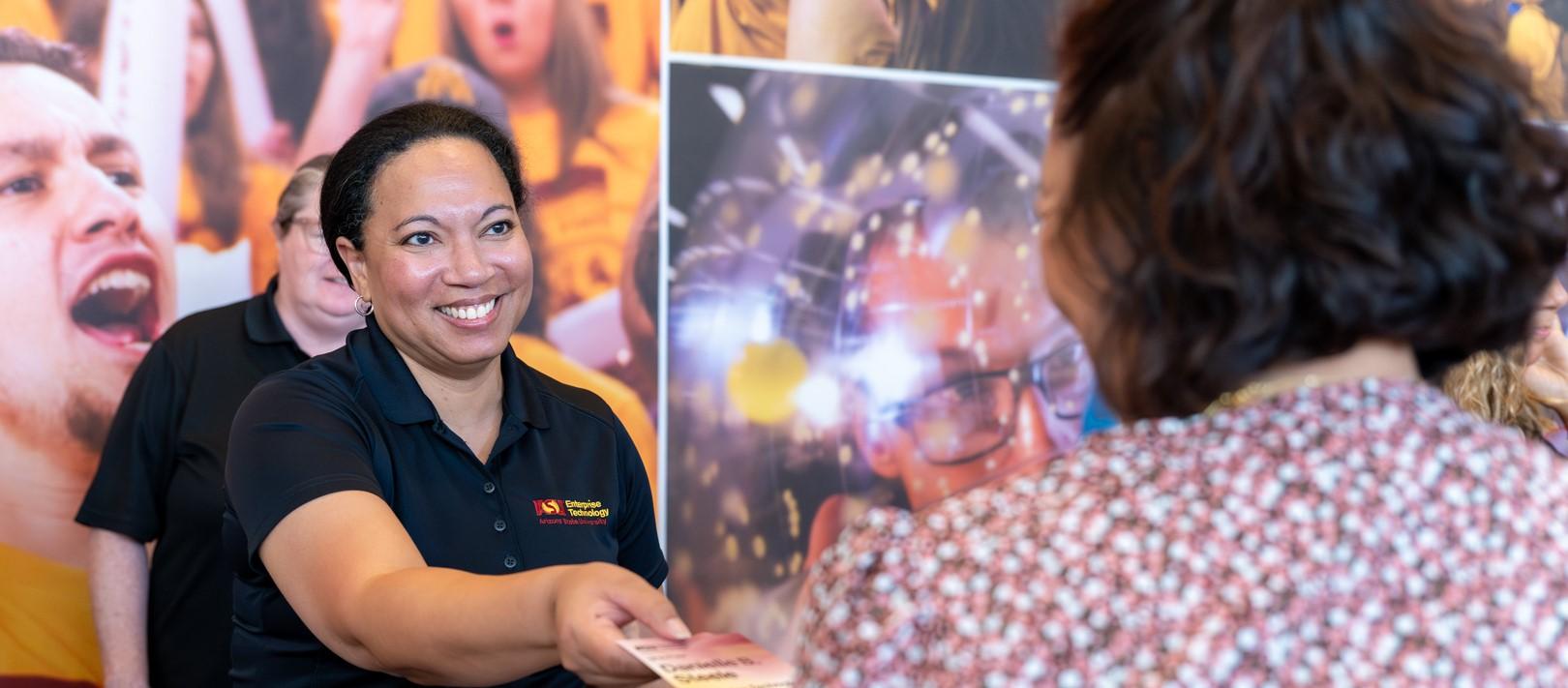 A staff member smiles and assists a fellow colleague as they check-in for Empower, an annual event hosted by Enterprise Technology.